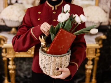 Smartphone mit geöffneter Gutscheinseite, daneben edel verpackte Geschenke in dunklem Rot mit goldenen Schleifen