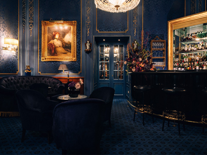 Elegant bar in deep blue tones with golden accents, lavish chandelier and ornate furnishings
