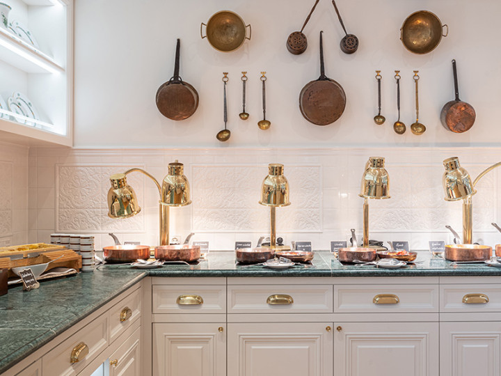 Stylishly furnished buffet with warm dishes under golden heat lamps, decorated with copper pans and kitchen utensils on the wall