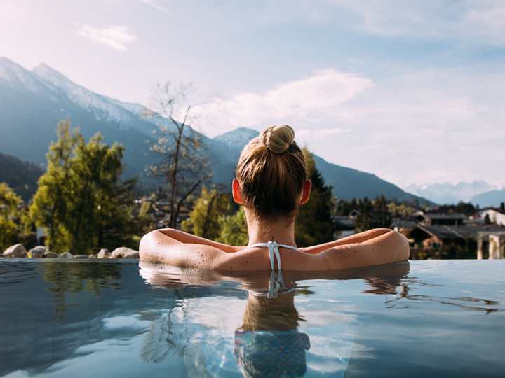 Woman relaxing in an infinity pool and enjoying the view of a mountain landscape