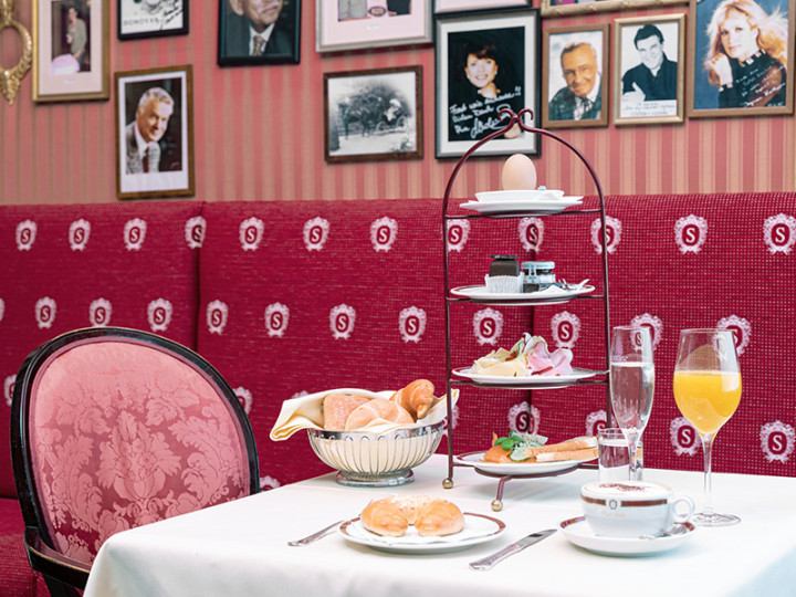 Stylish breakfast at the Hotel Sacher with a multi-tiered tiered stand, pastries, drinks and elegant red upholstery